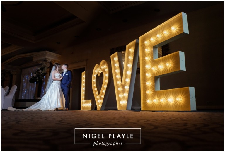 A stunning wedding photo capturing the joyful bride and groom in front of a beautifully illuminated love sign.