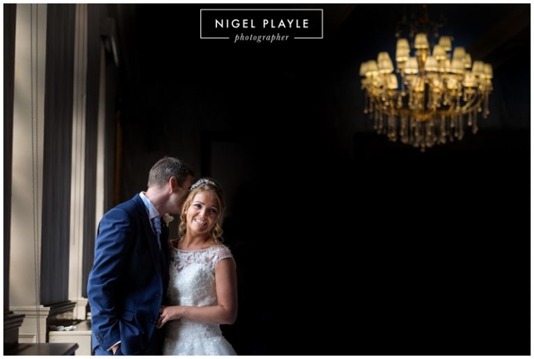 A couple posing in front of a chandelier for their wedding photograph.