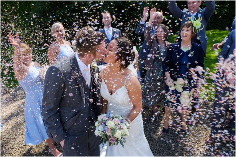 A mesmerizing wedding photograph capturing a blissful moment between a bride and groom as they share an unforgettable kiss, surrounded by jubilant confetti.
