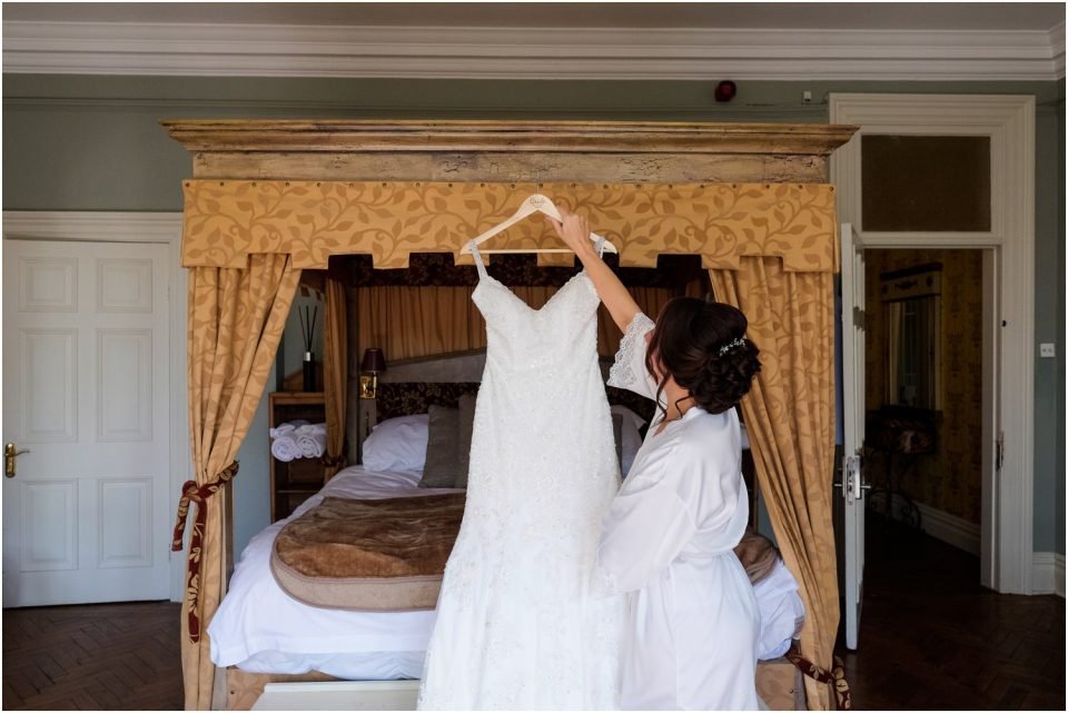 A bride is elegantly hanging her wedding dress on a four poster bed for a stunning wedding photography.