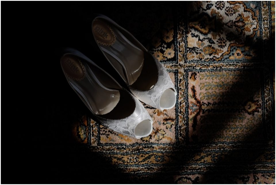 A pair of white wedding shoes on a rug captured in a stunning wedding photograph.