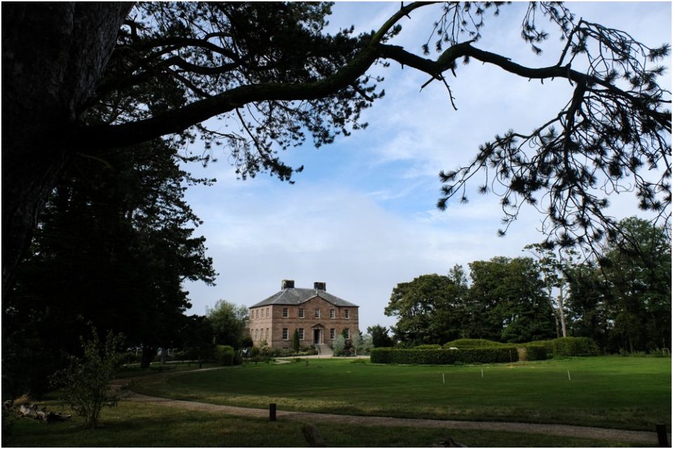 A grand mansion surrounded by tall trees, providing a perfect backdrop for a picturesque wedding photo.